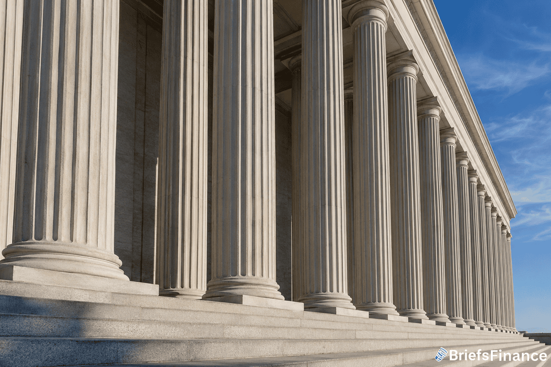A row of large stone columns supports the facade of a neoclassical building under a blue sky. Steps lead up to the entrance. BriefsFinance logo is in the bottom right corner.