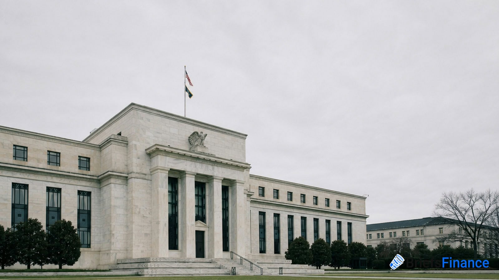 A large, white stone government building with columns and an American flag on top, set against a cloudy sky.