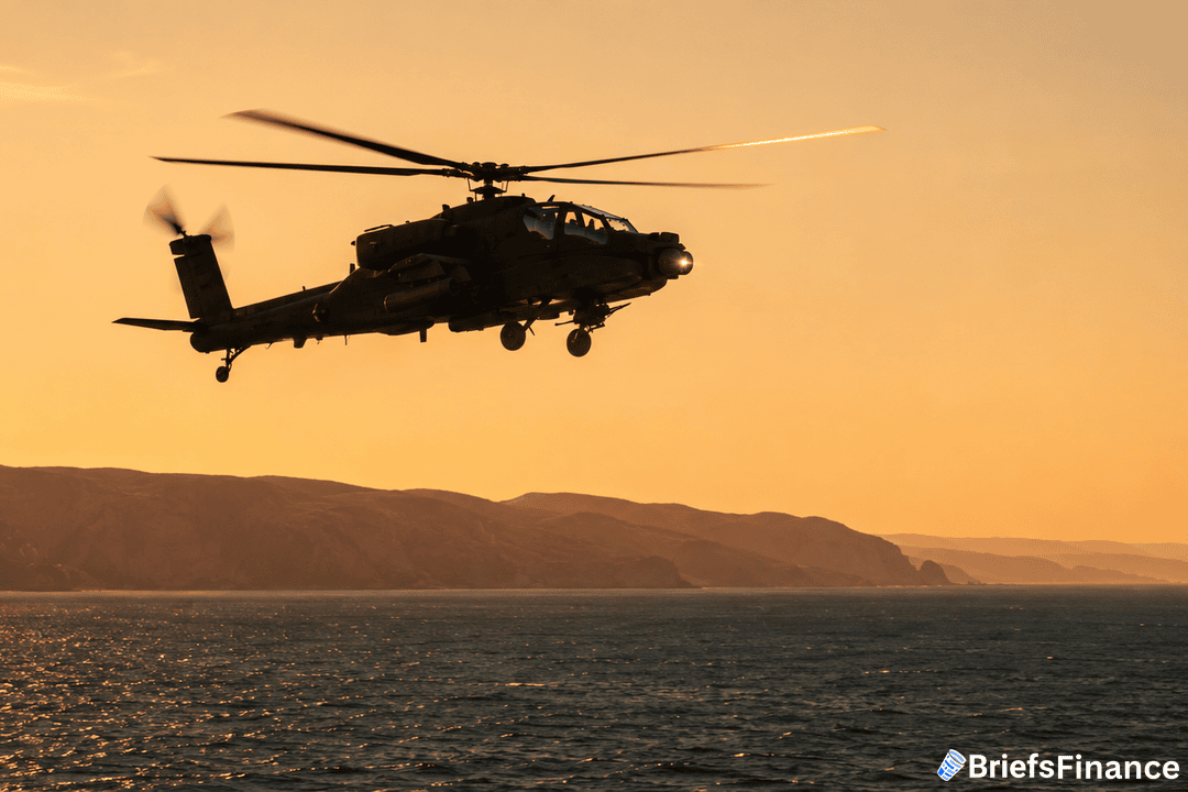 A military helicopter flies over the ocean at sunset, with rugged hills and a golden sky in the background. The helicopter is silhouetted against the light.