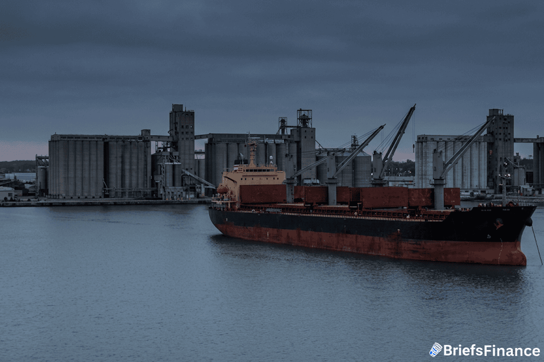 Bulk grain cargo ship anchored in a harbor at overcast dusk beside grain silos