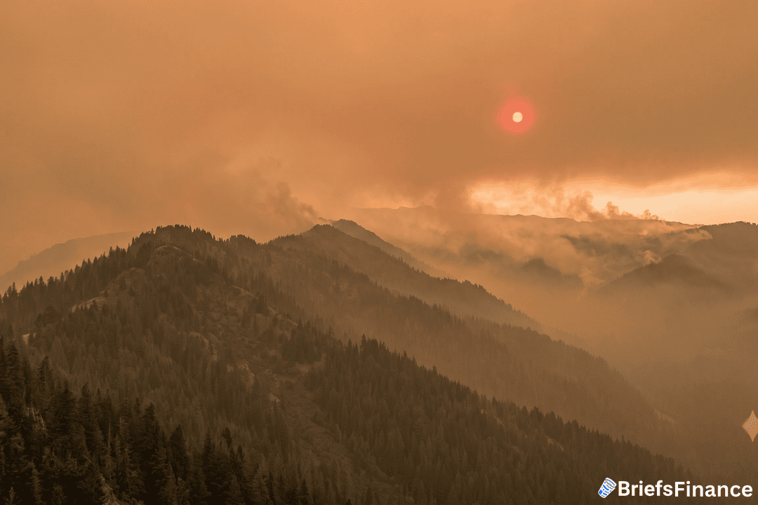 Wildfire smoke over a forested mountain ridge with a red sun